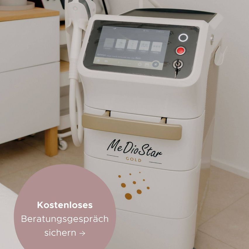 Eine weiße MeDioStar Gold Maschine mit einem digitalen Display und einem roten Knopf steht auf einem gefliesten Boden. Die Maschine hat einen beigen Griff und einen Schlüsselschlitz. Ein rosa Kreis mit dem Text 'Kostenloses Beratungsgespräch sichern' befindet sich auf der linken Seite.