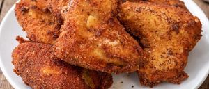 A plate of crispy fried chicken pieces on a wooden table with a bowl of ketchup and parsley in the background.