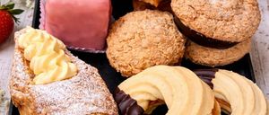 A black tray filled with various pastries including croissants, donuts, and a pink cake, surrounded by flowers and a strawberry.