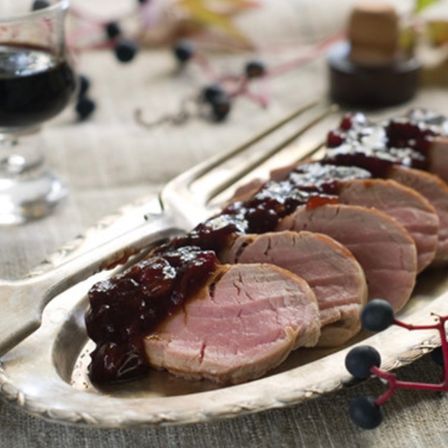 Scheiben von Schweinefilet mit Cranberry-Sauce auf einem silbernen Serviertablett mit einer Gabel und einem Glas Wein.