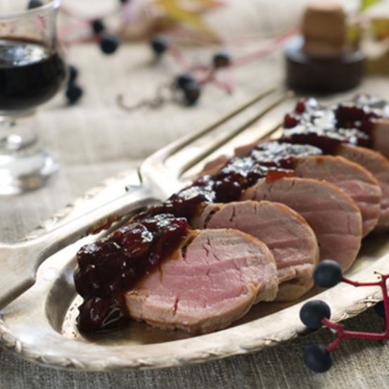 Scheiben von Schweinefilet mit Cranberry-Sauce auf einem silbernen Serviertablett mit einer Gabel und einem Glas Wein.