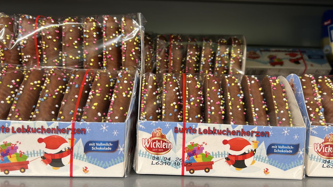 Mehrere Schachteln mit schokoladeüberzogenen Brezeln sind ausgestellt, mit bunten Streuseln. Die Schachteln haben festliche Motive, wobei eine Schachtel ein Pinguin- und Weihnachtsmann-Design hat.