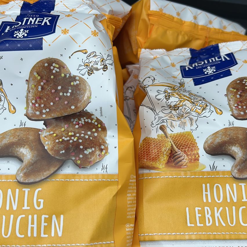 Zwei Tüten Honig Lebkuchen, ein honiggeschmackiger Lebkuchen mit herzförmigem Design und Streuseln, verpackt von Patiner. Die Tüten haben ein blau-weißes Etikett mit Illustrationen.