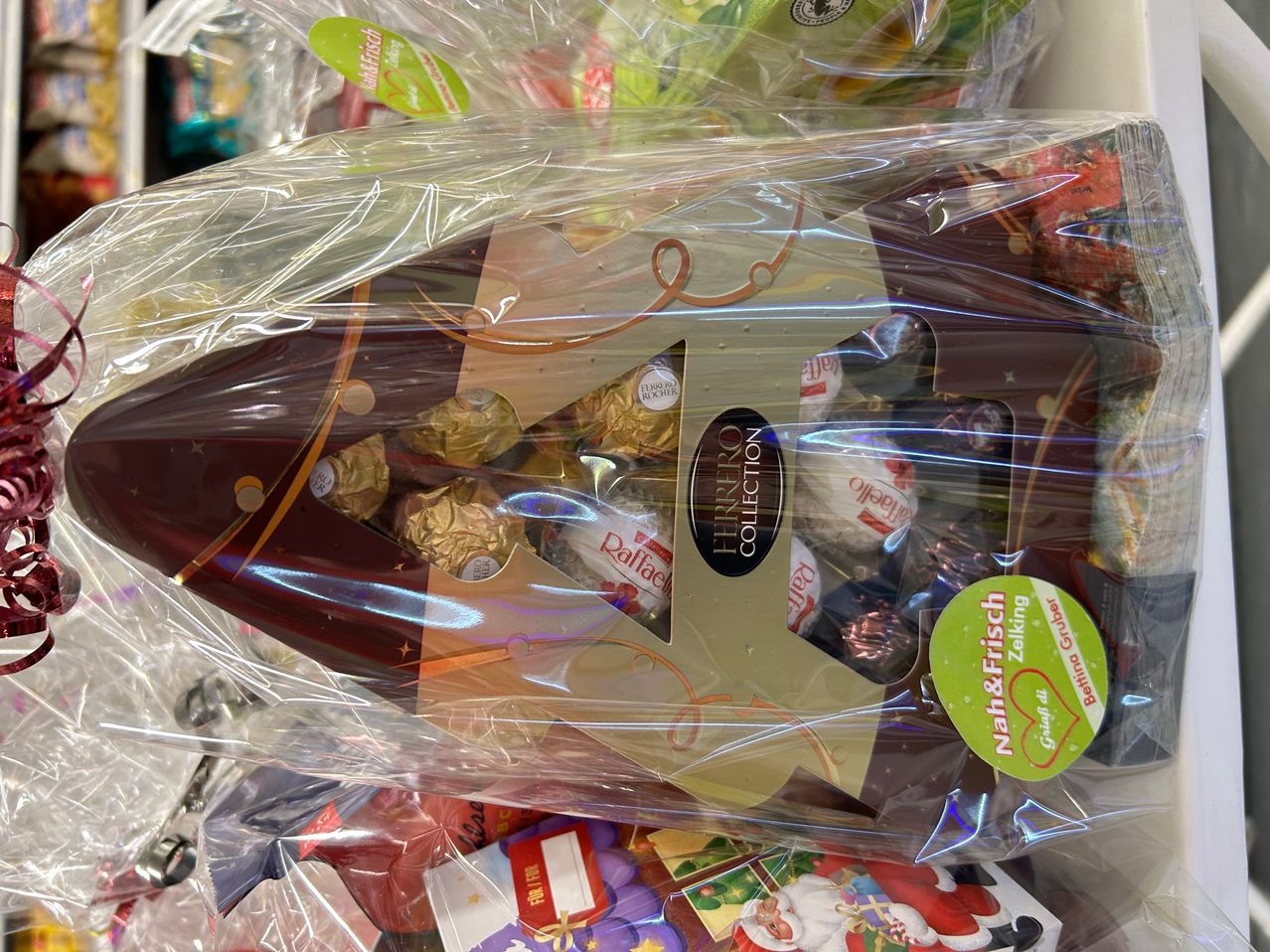 Ein durchsichtiger Plastikbeutel enthält ein Schokoladengeschenk mit festlichem Design, einschließlich Ferrero Rocher Schokoladen. Der Beutel ist teilweise geöffnet und zeigt einige Schokoladenstücke darin.