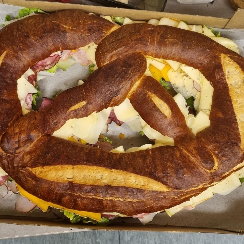 Ein großer Brezel aus Brot, gefüllt mit Käse und anderen Zutaten, in einer Pappschachtel.