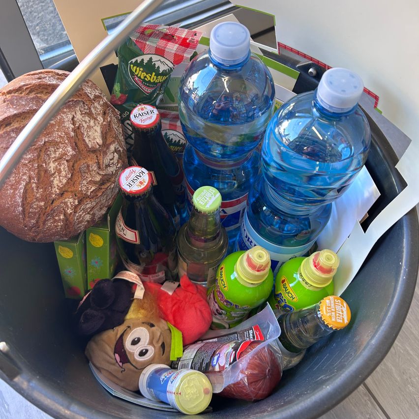 A bucket filled with various items including bread, bottles of water, juice, and snacks.