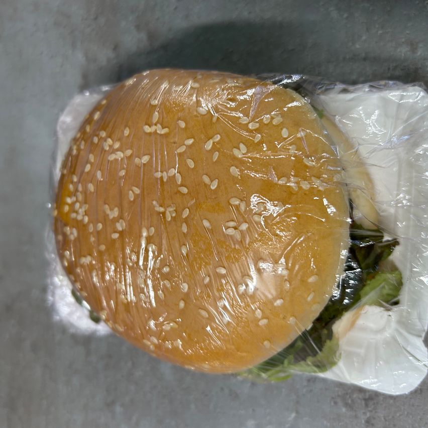 Ein Burger mit Sesamkörnern auf der oberen Brötchenhälfte ist in Plastik verpackt.