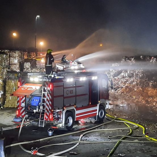 Ein Feuerwehrmann sprüht Wasser aus einem Feuerwehrwagen auf einen brennenden Abfallhaufen in der Nacht.