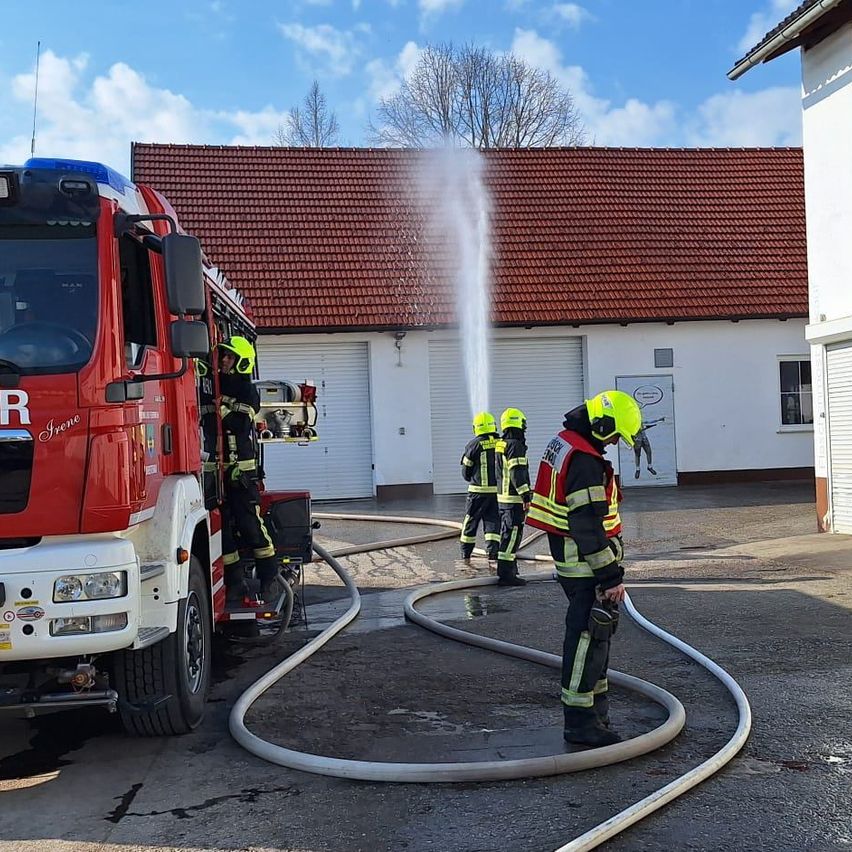 Ein Feuerwehrauto steht in der Nähe eines Gebäudes. Ein Feuerwehrmann sprüht Wasser aus dem Schlauch.