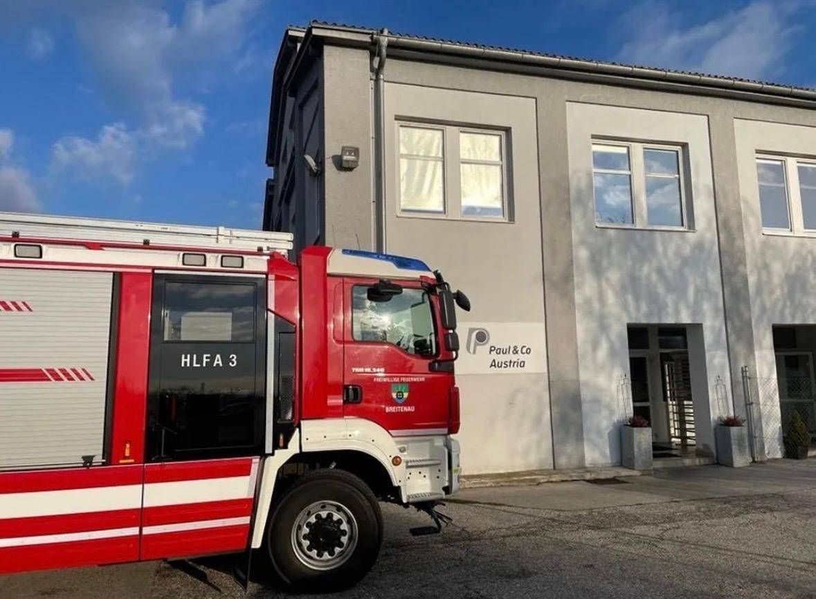 Ein roter Feuerwehrwagen mit der Aufschrift HLFa 3 steht vor einem Gebäude mit dem Schild Paul & Co Austria.