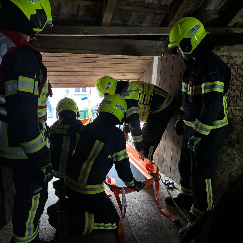 Feuerwehrleute in Schutzkleidung üben eine Rettung in einer Scheune. Vier Feuerwehrleute mit Helmen und gelben Westen, einer auf einer Trage.