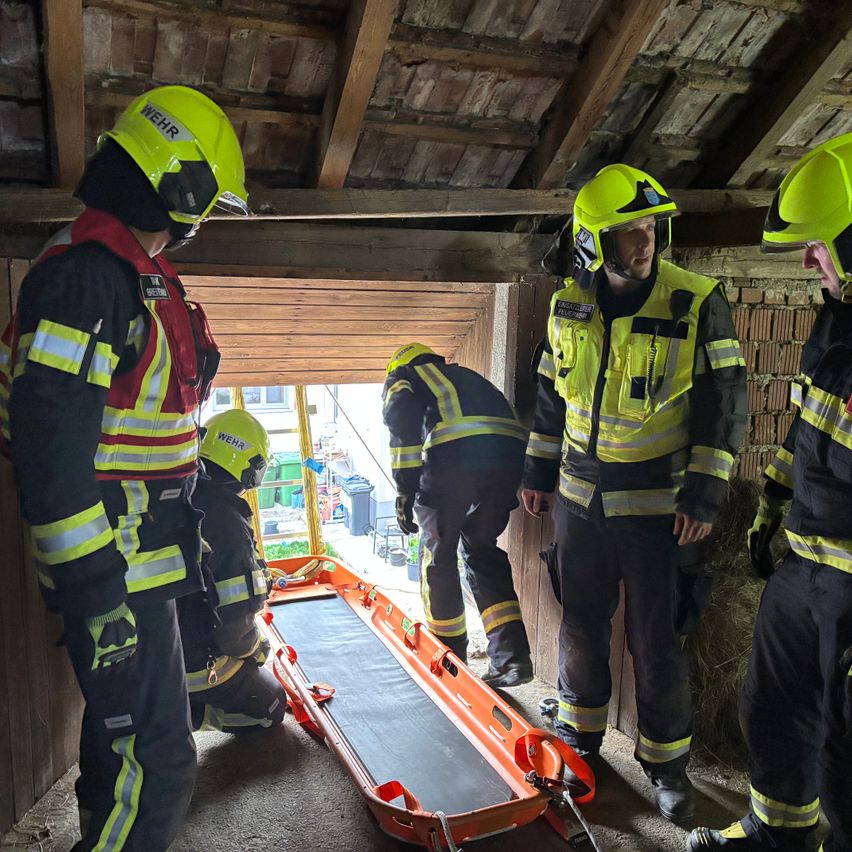 Eine Gruppe von Feuerwehrleuten in gelben Helmen und Schutzanzügen bereitet sich auf eine Rettung vor. Ein orangefarbener Krankenwagen liegt auf dem Boden.