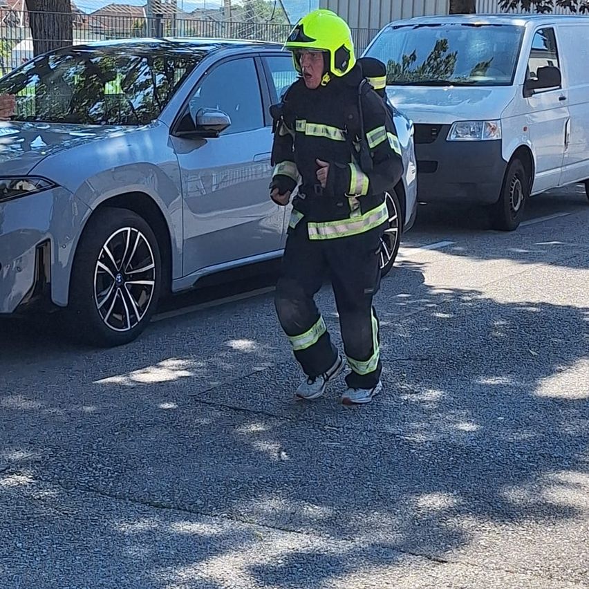 Ein Feuerwehrmann in einem grünen Helm und schwarzem Uniform mit reflektierenden Streifen läuft neben einem Auto auf einer Straße.