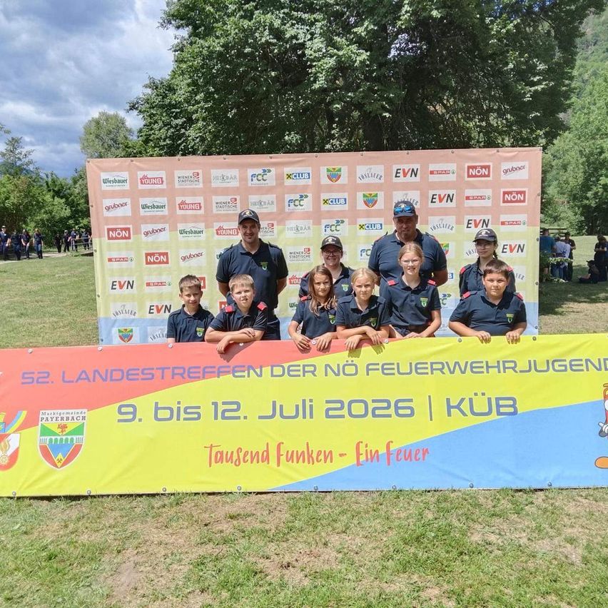 Eine Gruppe junger Menschen und Erwachsener in blauen Uniformen posiert für ein Foto vor einem großen Banner mit Logos und Text in Deutsch.