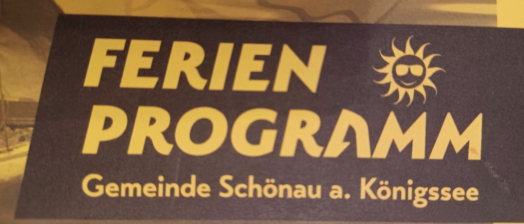 Ein Schild für Ferien Programm, wahrscheinlich ein Zeitplan für Gemeindeveranstaltungen, zeigt ein Sonnenlogo auf der rechten Seite. Der Hintergrund ist braun.