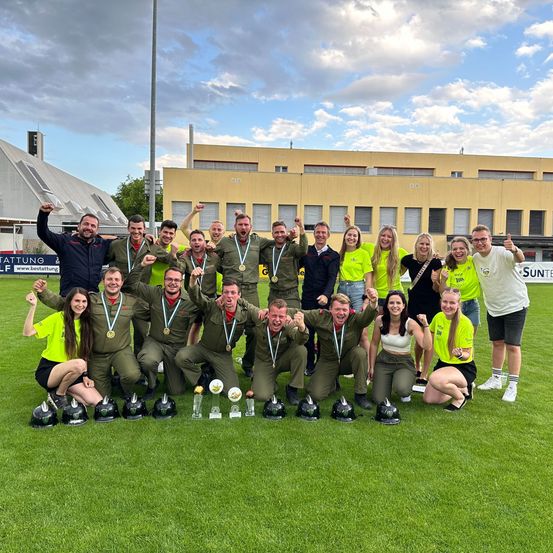 Eine Gruppe von Menschen in grünen und gelben Uniformen posiert für ein Foto auf einem Feld mit Trophäen.