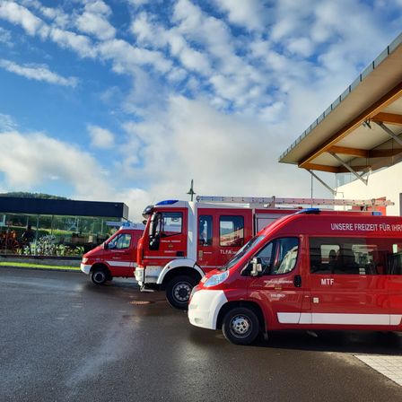 Drei rote Feuerwehrfahrzeuge sind vor einem Gebäude unter einem bewölkten Himmel geparkt.