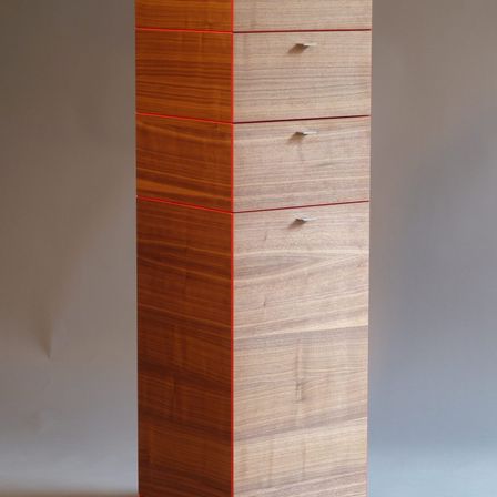 Ein vertikaler Holzschrank mit fünf Schubladen, jede mit einem roten Rand, vor einem grauen Hintergrund.