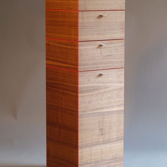 Ein vertikaler Holzschrank mit fünf Schubladen, jede mit einem roten Rand, vor einem grauen Hintergrund.