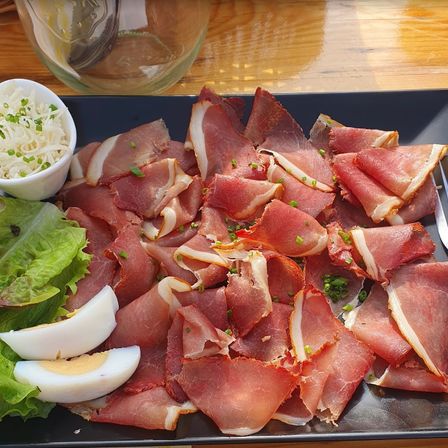 Ein schwarzer Teller mit Prosciutto-Schinken, Salat und gekochten Eiern. Ein Glas mit Wasser und ein Glas mit einem Löffel auf dem Tisch.