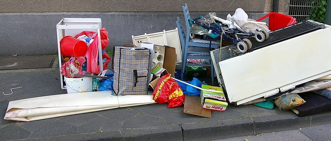 Ein Haufen verschiedener Gegenstände, darunter ein Kühlschrank, ein Kinderwagen, ein Aufbewahrungskasten und andere Haushaltsgegenstände, ist auf dem Bürgersteig abgeladen.