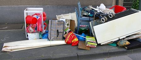 Ein Haufen verschiedener Gegenstände, darunter ein Kühlschrank, ein Kinderwagen, ein Aufbewahrungskasten und andere Haushaltsgegenstände, ist auf dem Bürgersteig abgeladen.