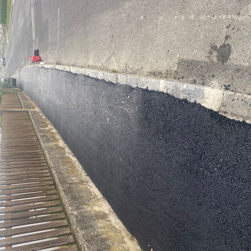 Ein neuer schwarzer Asphaltweg wird an der Seite einer Straße mit einem Holzzaun gepflastert.
