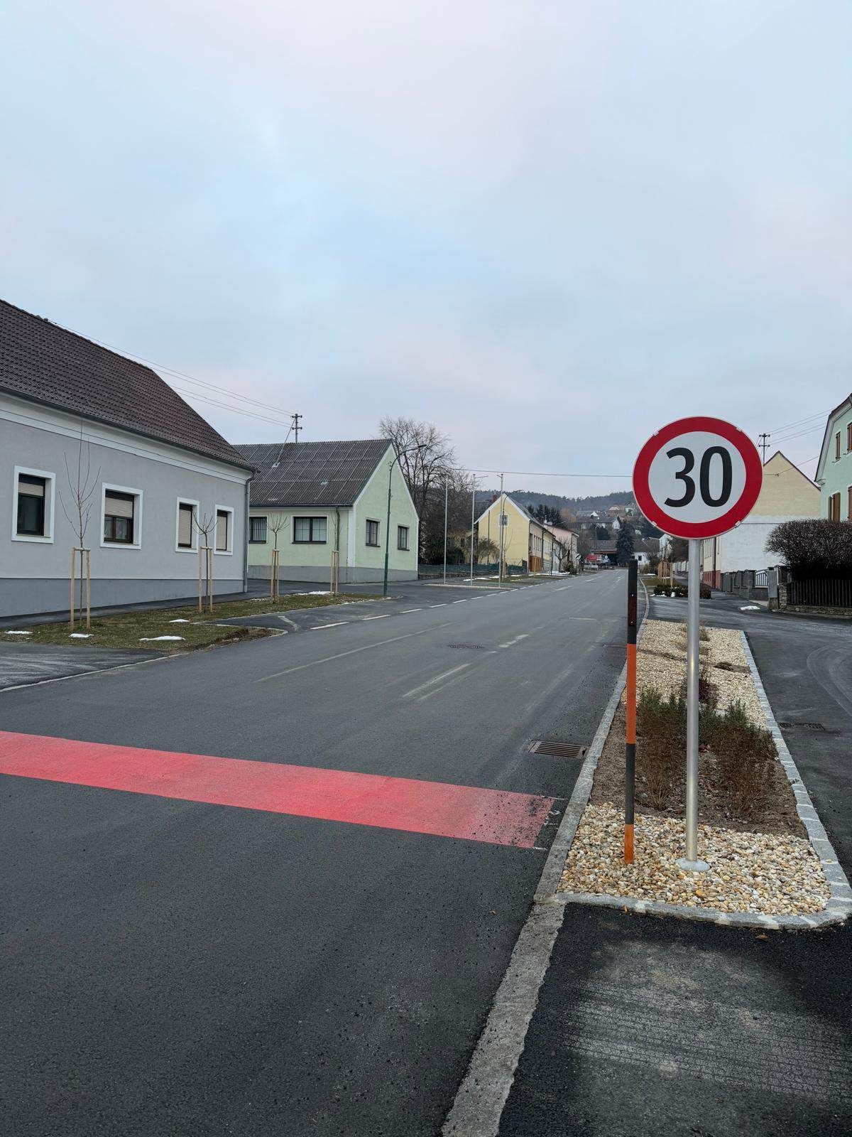 Eine leere Straße mit einem 30 km/h Geschwindigkeitsbegrenzungsschild und einer roten Linie auf der Straße, mit Häusern auf beiden Seiten.