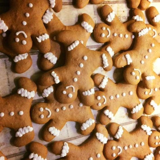 Eine Nahaufnahme von Lebkuchen mit weißer Zuckerguss verziert, Augen, Nasen und Lächeln. Die Kekse liegen auf einer Holzoberfläche, möglicherweise einem Tisch.