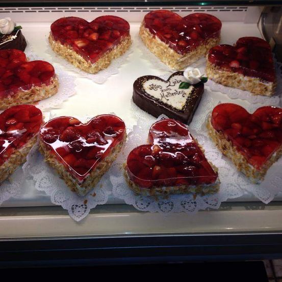 Eine Ausstellung von herzförmigen Desserts, einschließlich Schokoladen- und Erdbeergelatinekuchen, auf einem weißen Tablett mit Spitzenunterlage angeordnet.