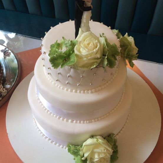 Eine dreistufige weiße Hochzeitstorte mit Perldekorationen und weißen Rosen oben und unten.