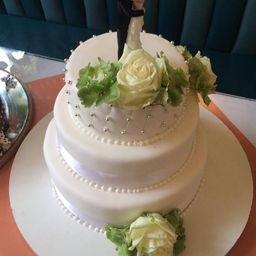 Eine dreistufige weiße Hochzeitstorte mit Perldekorationen und weißen Rosen oben und unten.