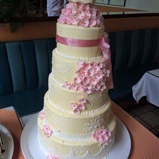 Ein vierstöckiger Hochzeitskuchen mit rosa Blüten und einer rosa Schleife auf einem weißen Teller in einem Restaurant.