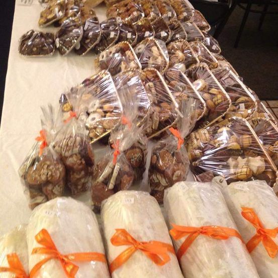 Ein Tisch mit einer Auswahl an Desserts, einschließlich verpackter Schokoladen und Gebäck, teilweise in Plastik, alle mit orangefarbenen Schleifen verziert. Der Tisch ist mit einem weißen Tuch bedeckt.