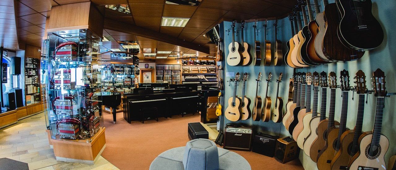 Ein Musikgeschäft mit Gitarren an der Wand und einem Klavier in der Ecke. Ein blauer gepolsterter Sitz ist in der Mitte.