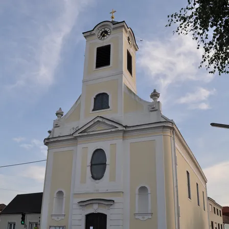 Eine weiße Kirche mit einem Glockenturm und Bogenfenstern steht an einer Straße. Ein Verkehrslicht und ein Gebäude befinden sich auf der linken Seite.