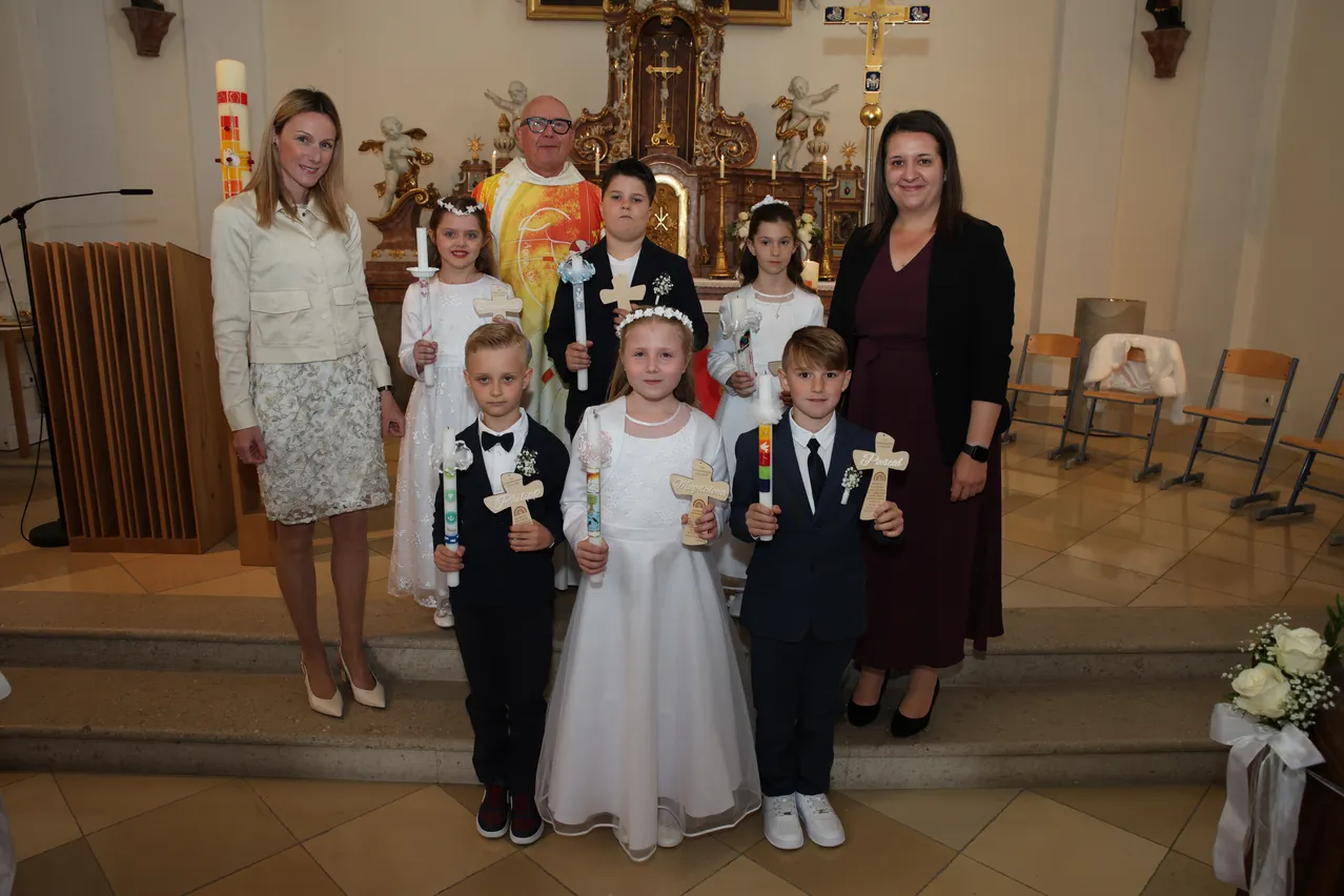 Eine Gruppe von Kindern und Erwachsenen steht vor einem Altar mit Kerzen in einer Kirche.