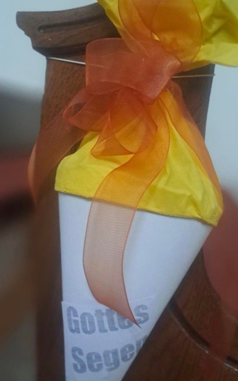 Ein weißer zylindrischer Gegenstand mit einem gelben Dach und einer orangefarbenen Schleife darum. Die Schleife hat eine glänzende Textur.