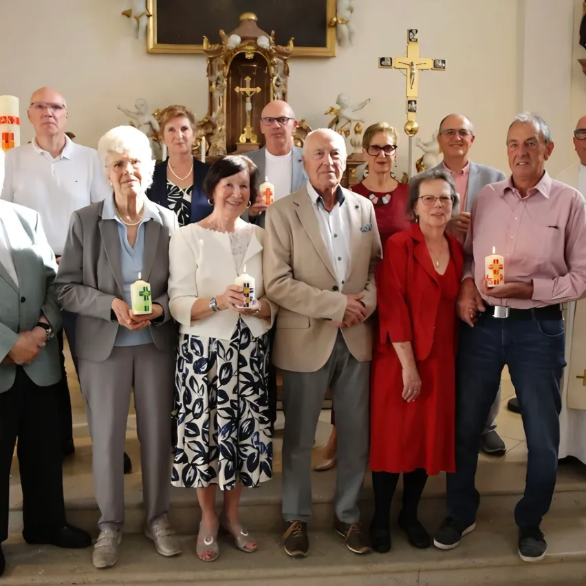 Eine Gruppe älterer Personen, gekleidet in formelle Kleidung, steht auf den Stufen einer Kirche und hält Kerzen. Sie scheinen für ein Foto zu posieren.