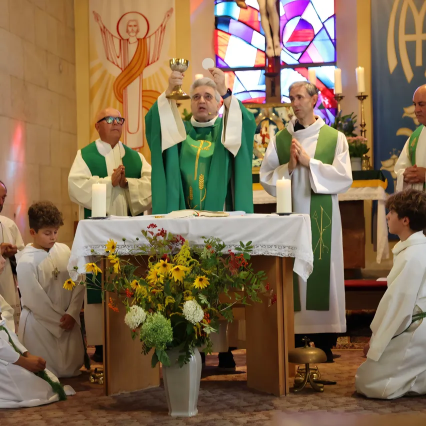 Ein Priester erhebt während einer Kirchenzeremonie einen Kelch, umgeben von anderen Geistlichen und Messdienern.