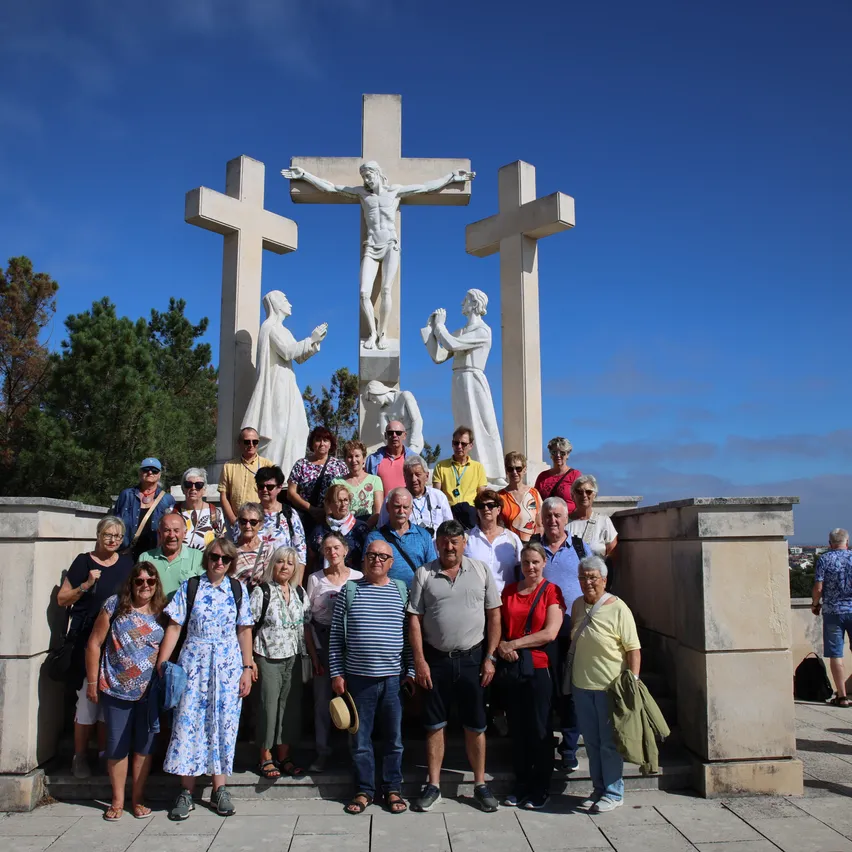Eine Gruppe von Menschen posiert für ein Foto vor einem großen Kreuzmonument unter einem klaren blauen Himmel.