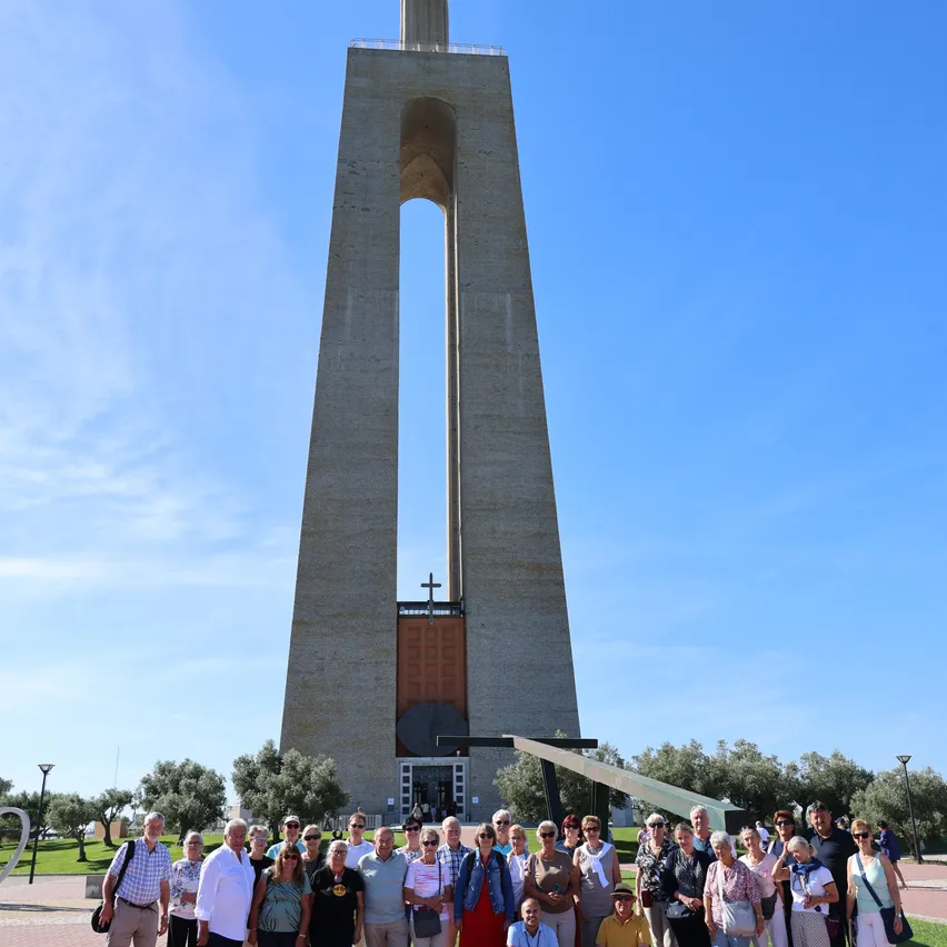 Eine Gruppe von Menschen posiert für ein Foto vor einem großen Betonmonument mit einem Kreuz auf der Spitze.