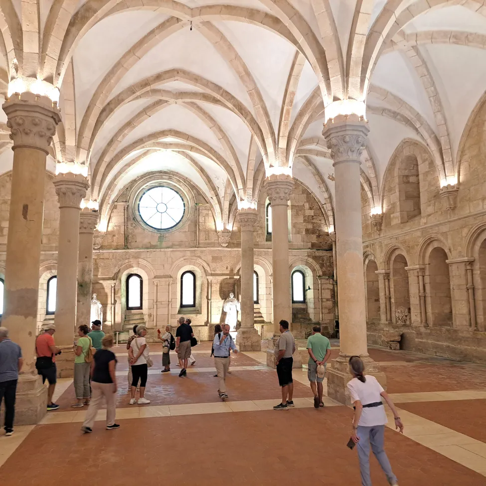 Besucher erkunden das Innere eines historischen Gebäudes mit gewölbten Decken, Steinsäulen und einem zentralen Rundfenster.