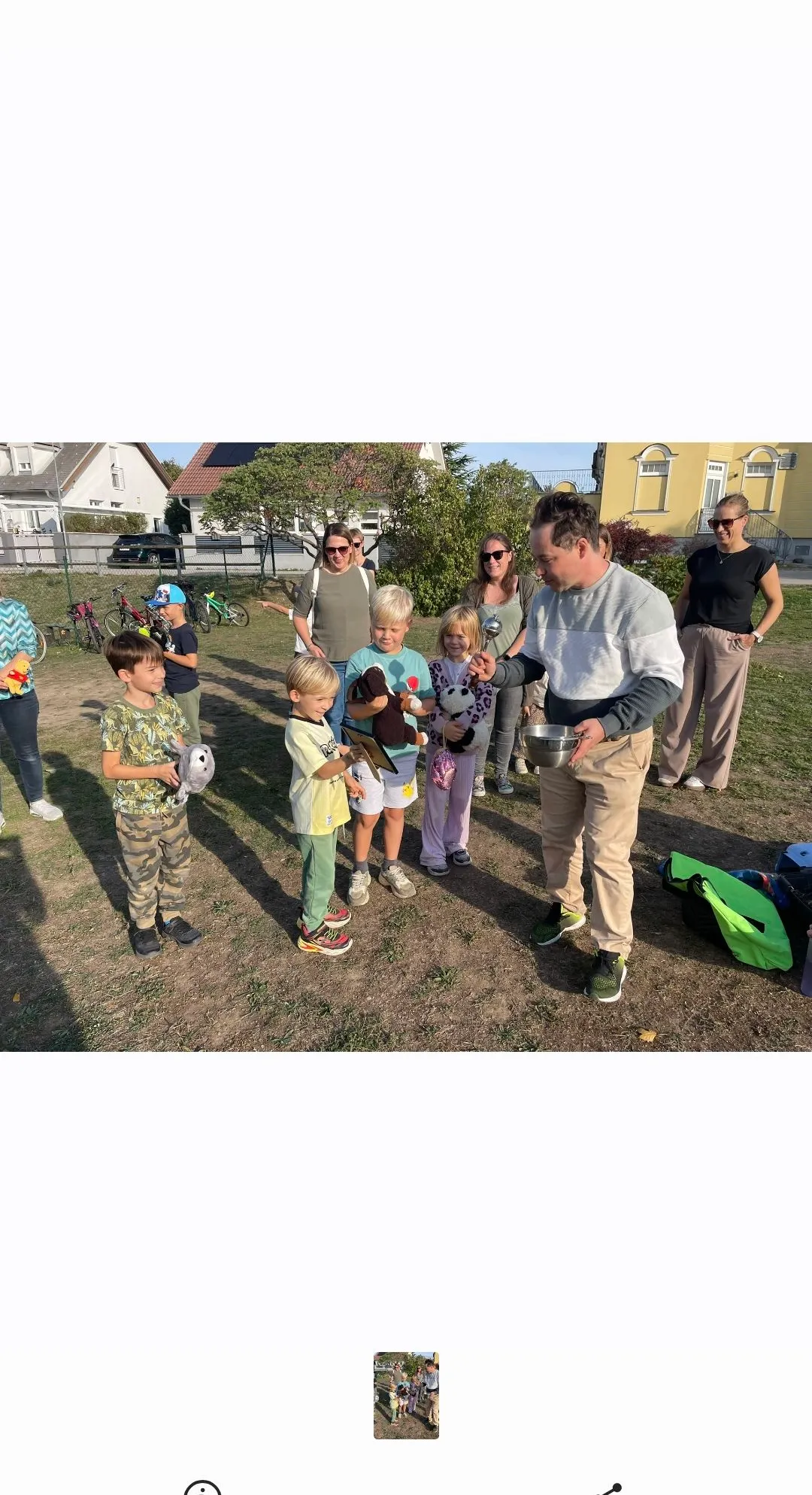 Eine Gruppe von Kindern und Erwachsenen steht auf einem Feld. Der Mann vorne hält ein Kuscheltier und scheint mit den Kindern zu sprechen.
