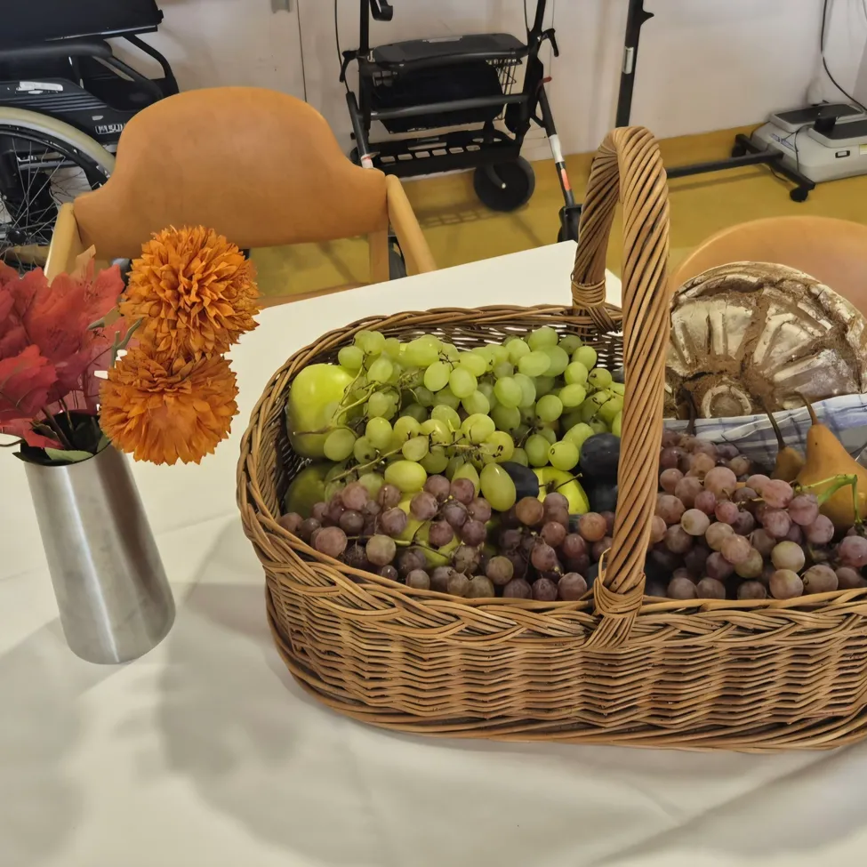 Ein Korb voller Trauben, Birnen und Brot auf einem Tisch mit einem Blumenvase.