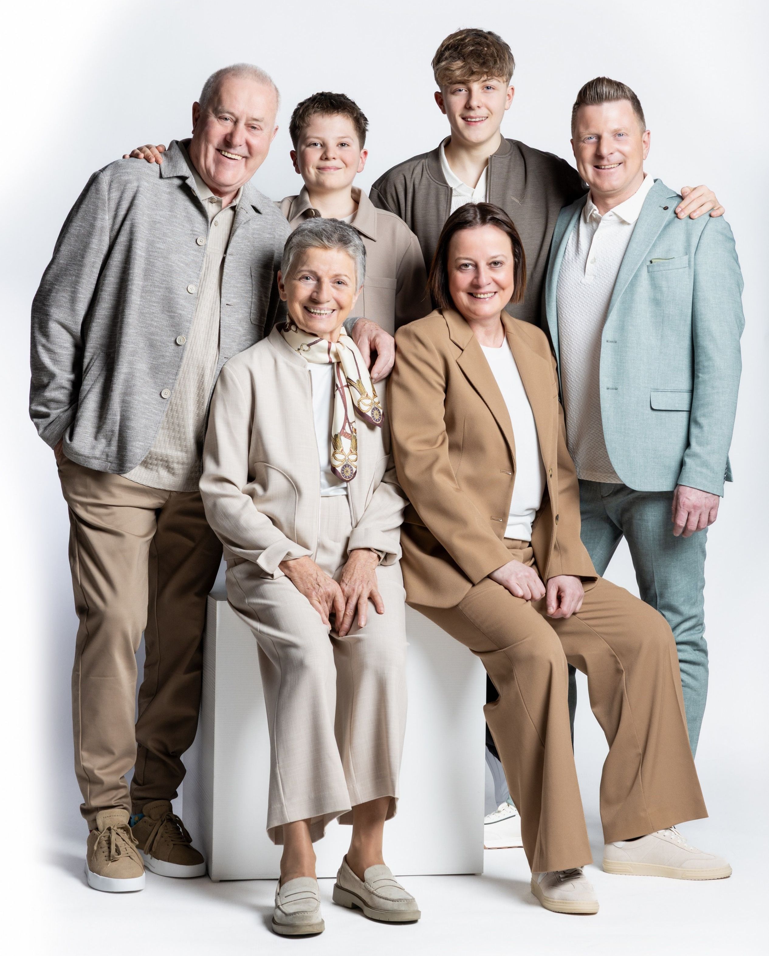 A group of family members posing for a picture, with two elderly people sitting, two standing behind them, and two men standing on either side.