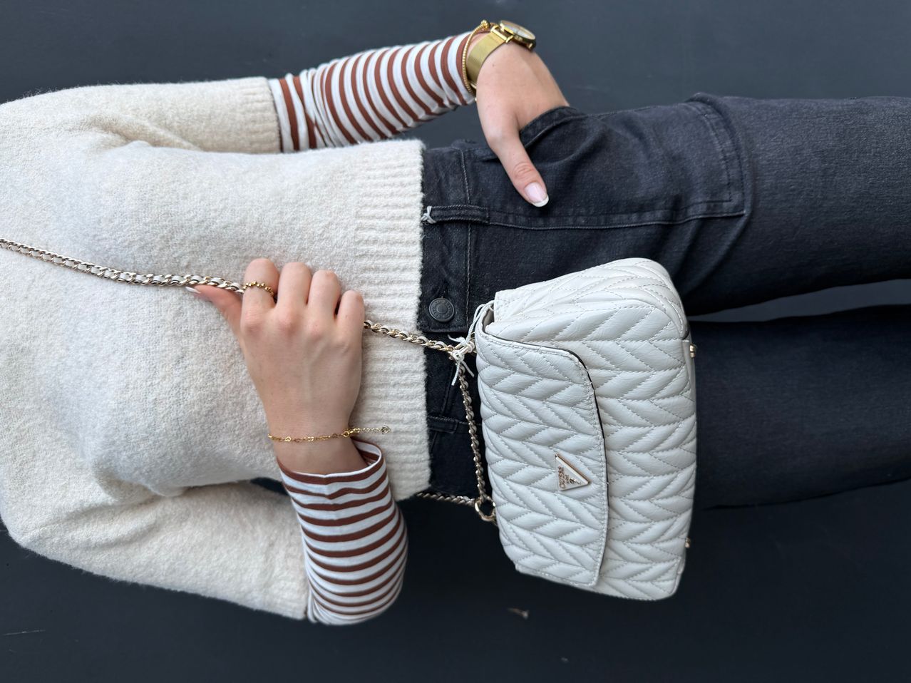 Eine Frau in einem weißen Pullover und einem gestreiften Langarmshirt hält eine weiße gesteppte Prada-Tasche.