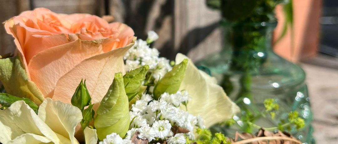 Eine Nahaufnahme eines Blumenstraußes mit Rosen, platziert in einer grünen Vase, mit einem hölzernen Hintergrund.