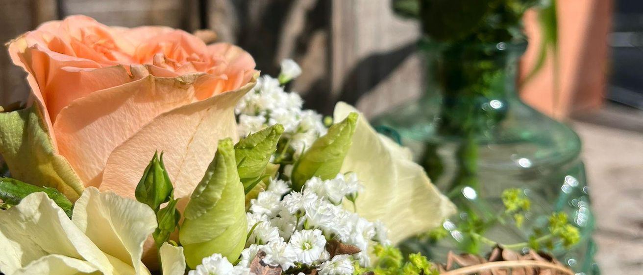 Eine Nahaufnahme eines Blumenstraußes mit Rosen, platziert in einer grünen Vase, mit einem hölzernen Hintergrund.