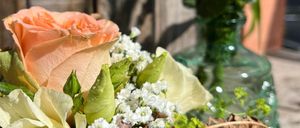 Eine Nahaufnahme eines Blumenstraußes mit Rosen, platziert in einer grünen Vase, mit einem hölzernen Hintergrund.